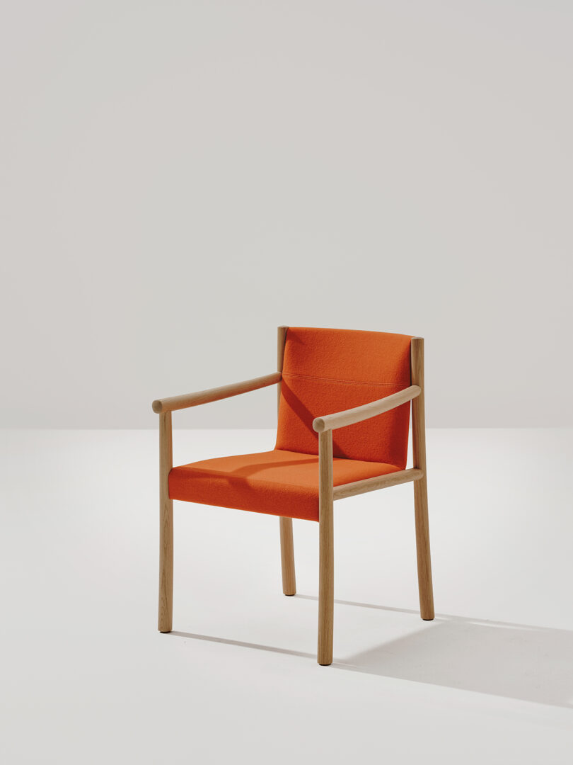 A Kata Chair by Arper with armrests, featuring orange upholstery on the seat and backrest, is shown against a plain white background.