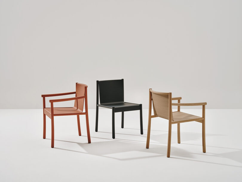 Three Kata Chairs of different colors (red, black, and light wood) are arranged in a minimalist setting against a neutral background.