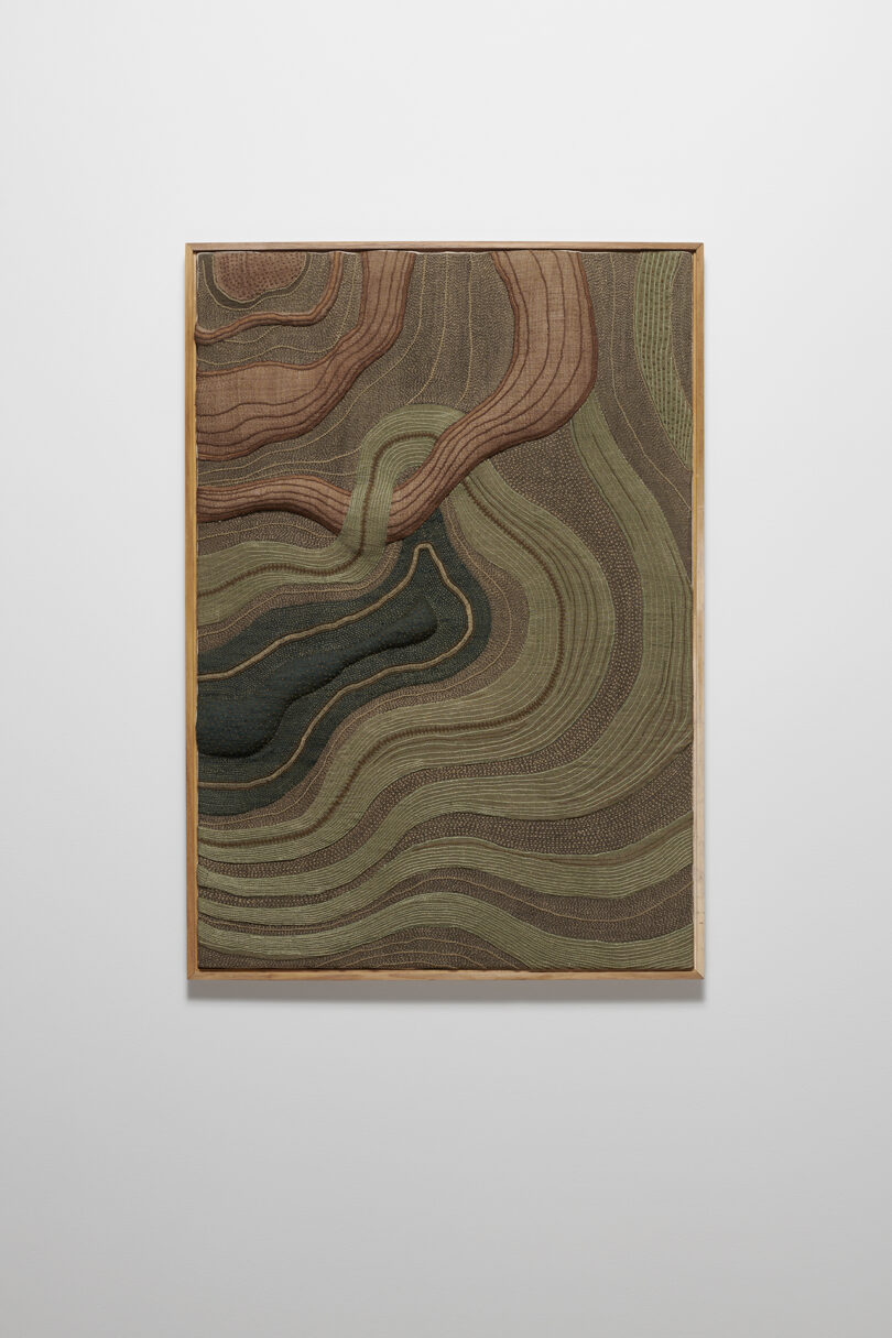 Framed artwork with wavy, layered patterns in shades of brown, green, and beige.