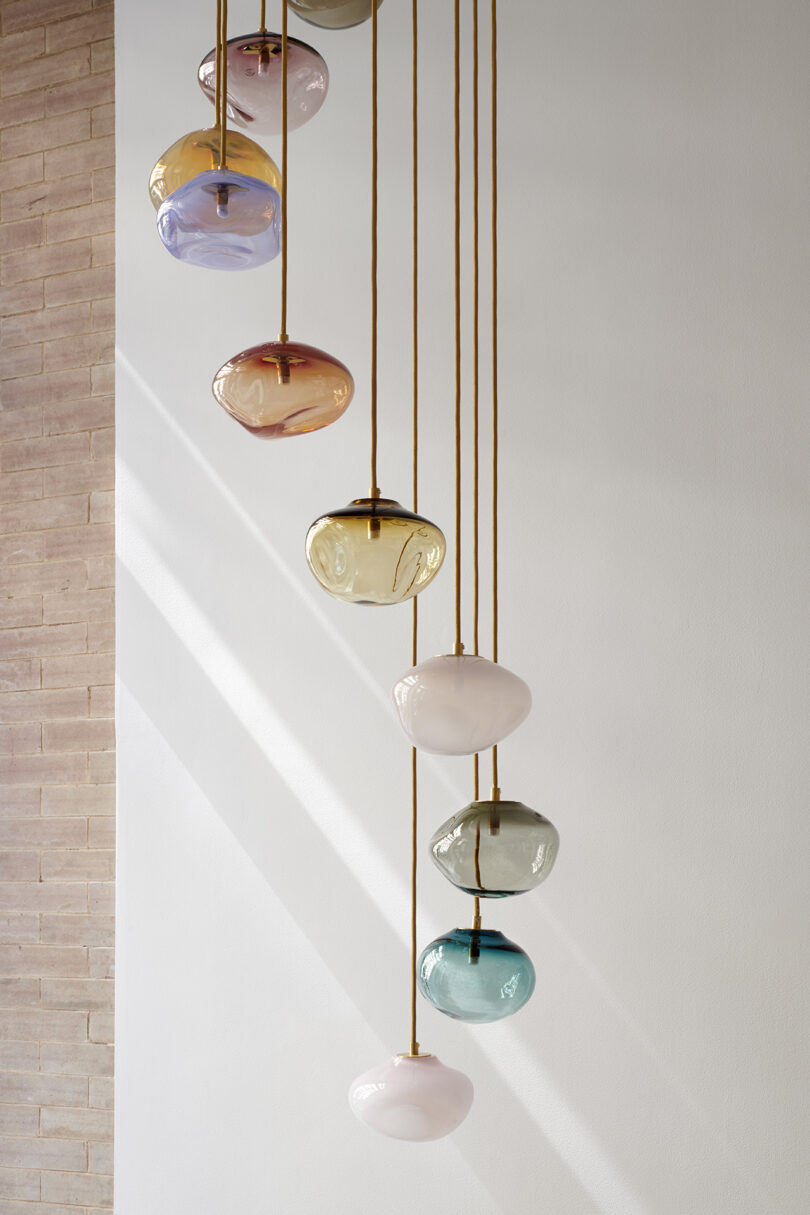 A series of colorful, round pendant lights hanging from the ceiling against a white wall and brick backdrop.