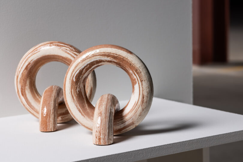 Two ceramic ring sculptures with a marbled design, resting on a white table in a minimalist setting