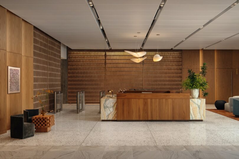 Modern hotel reception area with wooden and stone design, featuring a central desk, decorative lighting fixtures, and plants. Marble floor and geometric seating provide a contemporary ambiance.