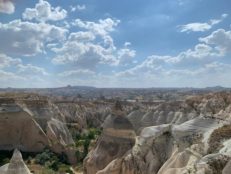 A panoramic view of Cappadocia's unique rock formations under a partly cloudy sky, with a distant landscape visible on the horizon.