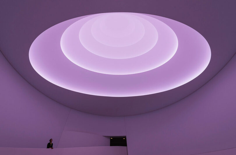 A person stands by a railing under a circular, layered ceiling with purple lighting.