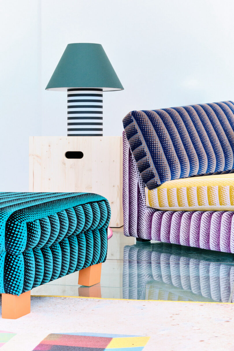 Colorful modern furniture set with a striped sofa, chair, and a lamp on a wooden table. Geometric patterns and vibrant colors stand out against a minimalistic backdrop