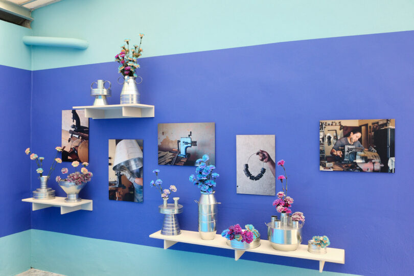 A blue wall displaying metal vases with colorful flowers, alongside photographs of crafting processes