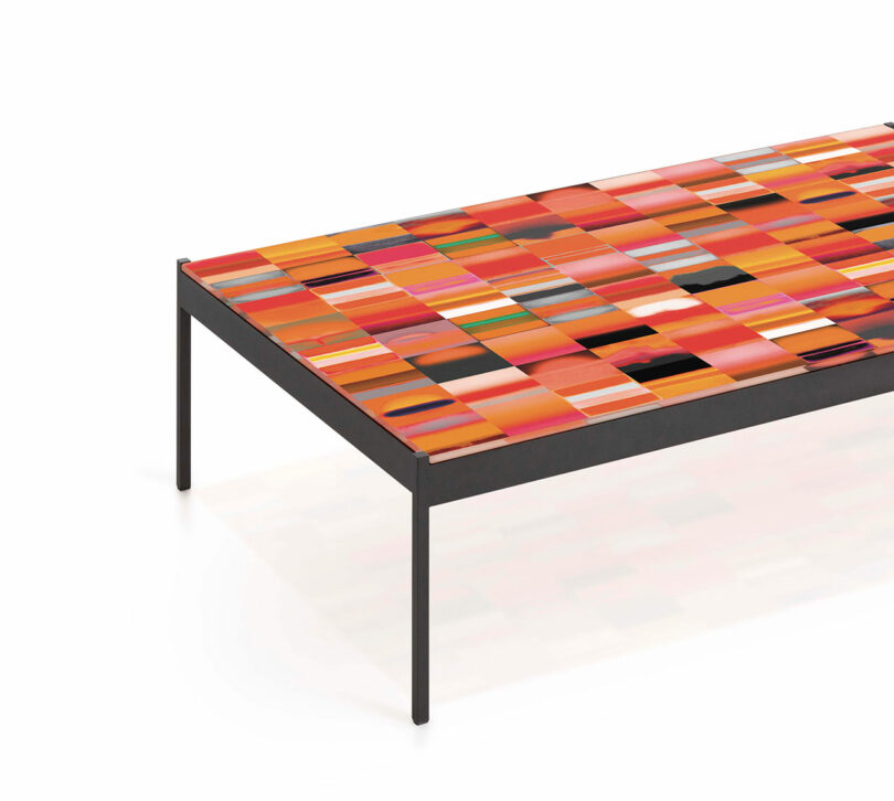 A table with a colorful, mosaic-like top featuring various shades of red, orange, and pink. It has a sleek, minimalist black metal frame and legs.