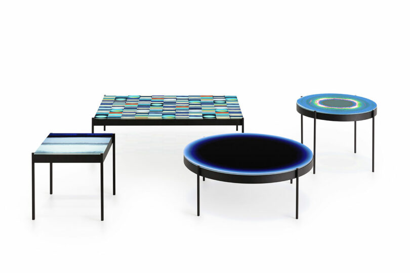 Four modern tables with colorful, artistic tops and slender legs are arranged on a white background.