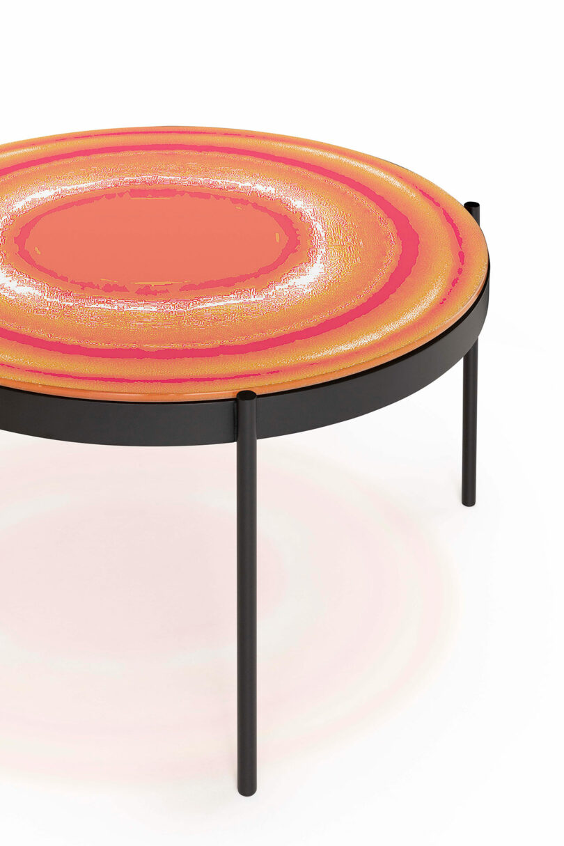 Round table with a vibrant, concentric circle pattern in shades of orange and red, supported by black metal legs.