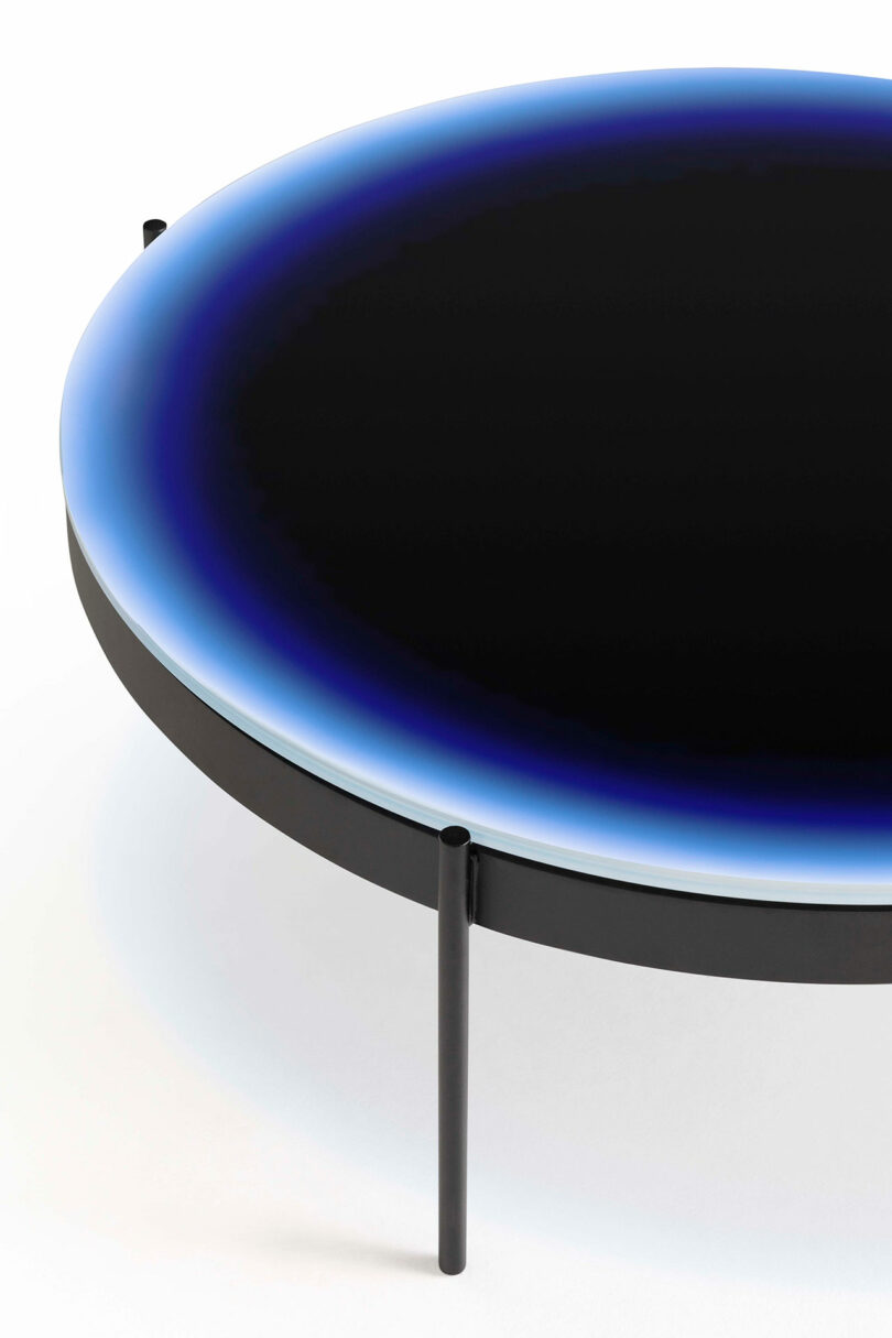 Round table with black top and gradient blue edge, supported by three slender black legs.