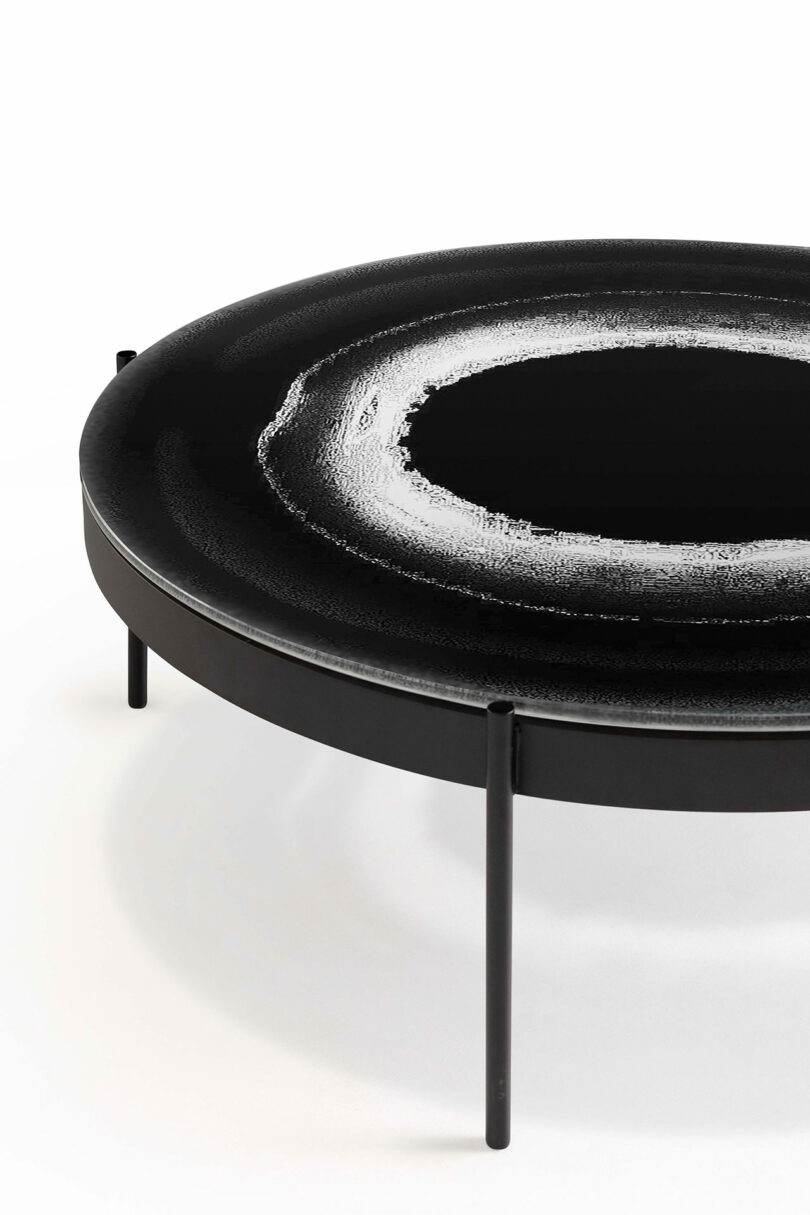 A round black table with a textured white ring design on the surface, supported by four slender legs.