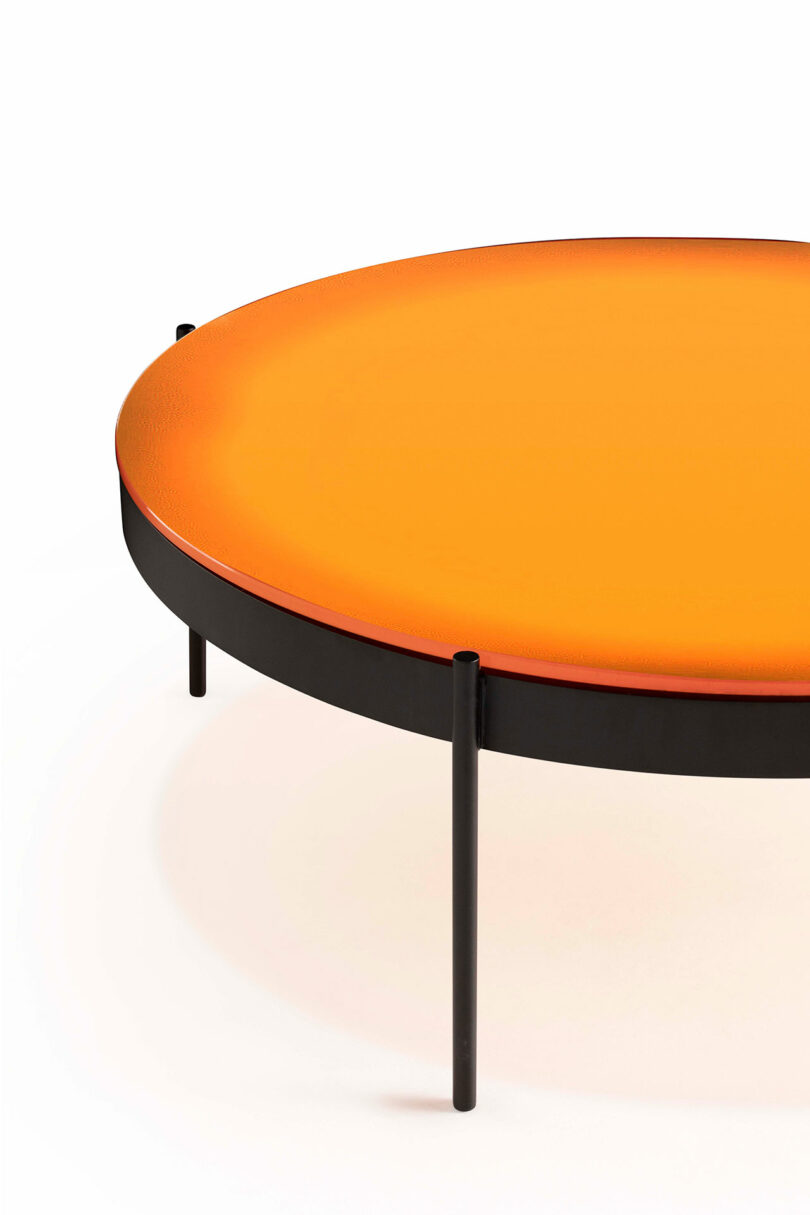 A round table with an orange top and black frame featuring three slim black legs.