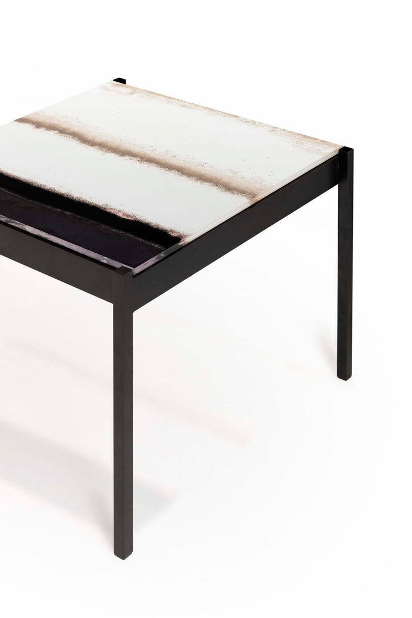 A modern square table with a black metal frame and a textured top featuring horizontal bands in white and black.