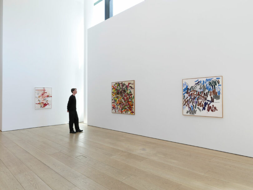 Man admires 3 paintings in gallery.