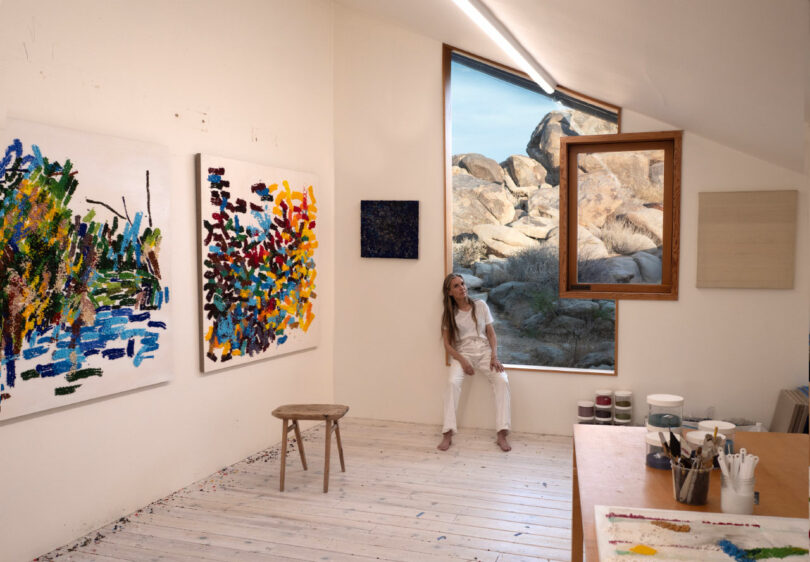 Artist sits on window frame in studio.