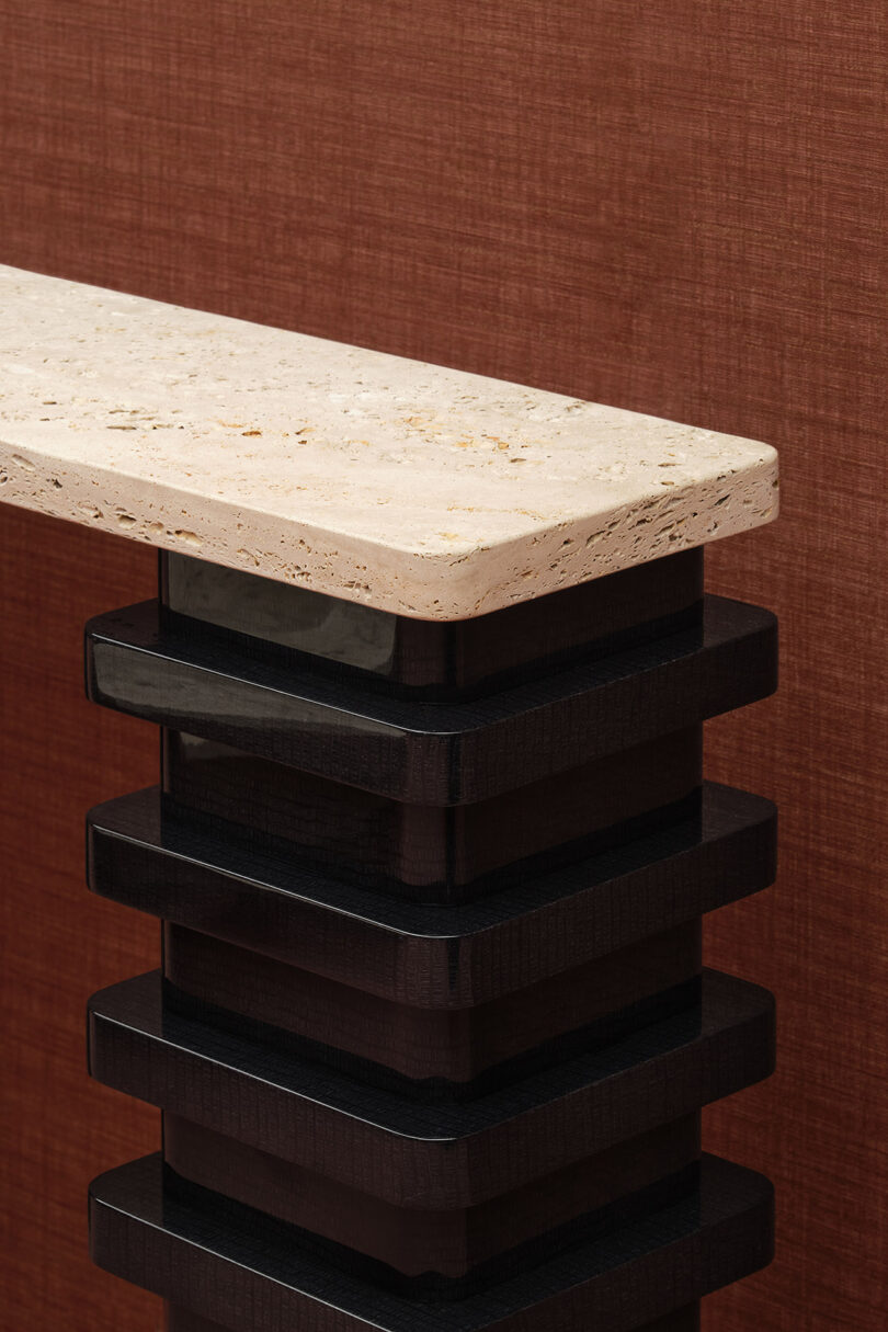 A stone tabletop rests on a stack of dark, glossy rectangular supports against a textured brown background.