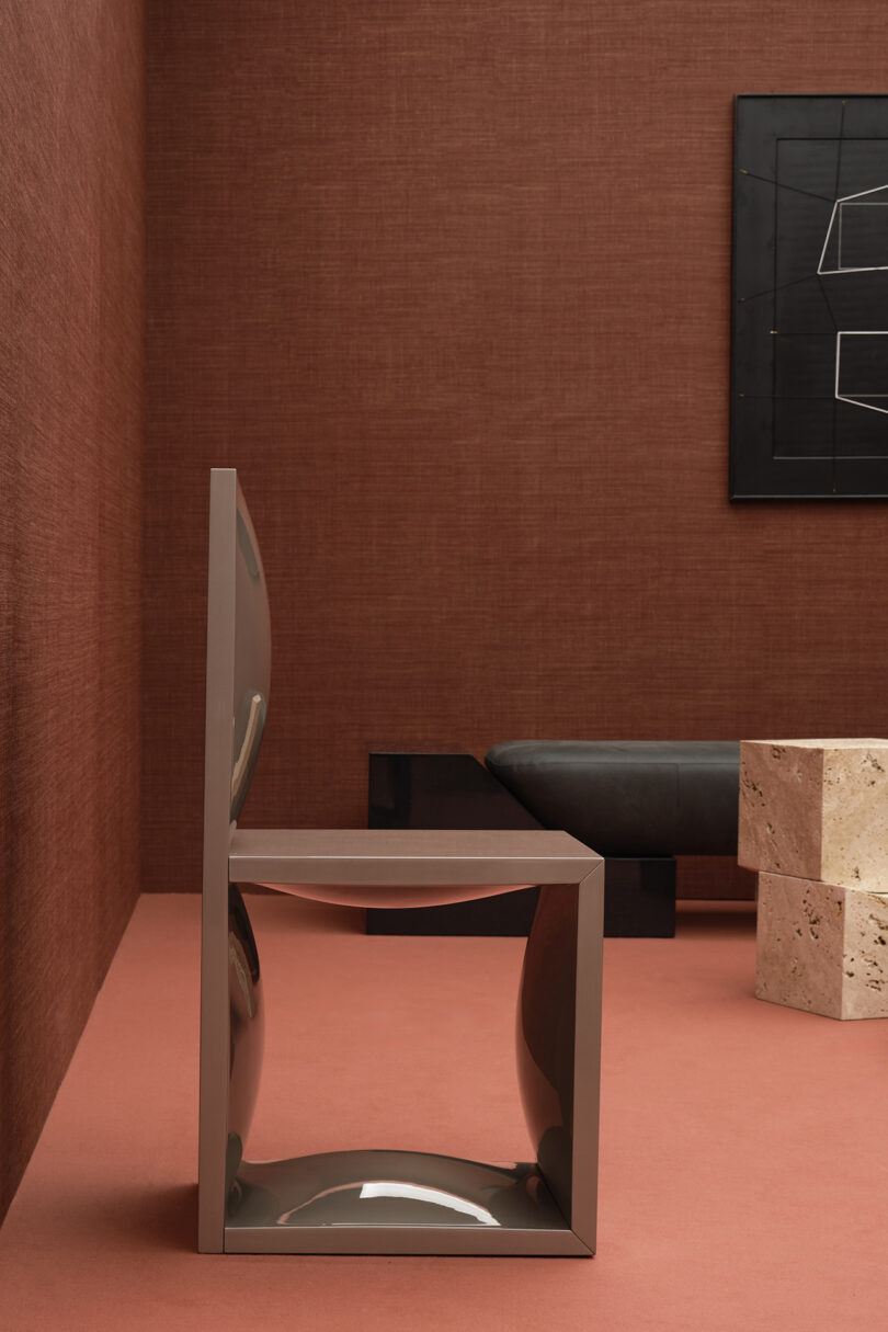 A modern room showcases a brown geometric chair, a stone table, and a black sofa. Marks of Existence Movimento is reflected in the black abstract artwork adorning the brown wall.