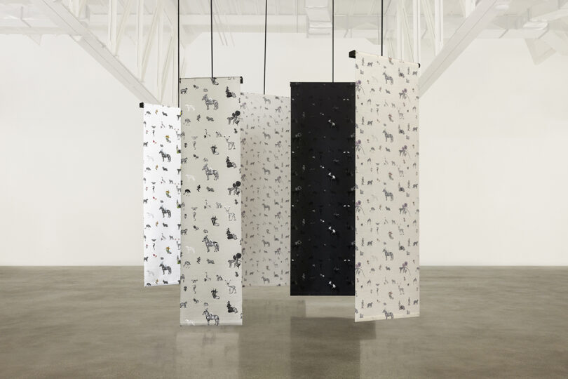 Hanging fabric panels with animal prints displayed in a minimalist gallery setting.