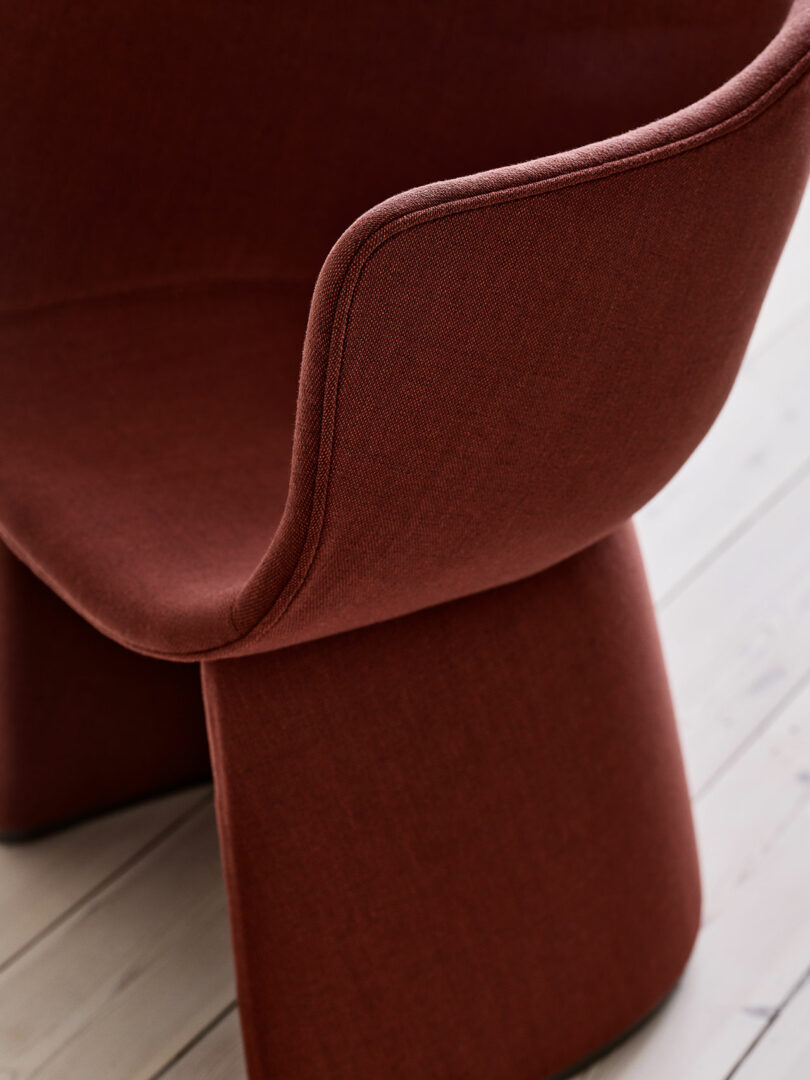 Close-up of a modern, rust-colored fabric chair on a light wooden floor.