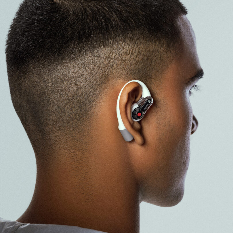 A person with short hair is wearing an ear-mounted device with a white loop and black earpiece.