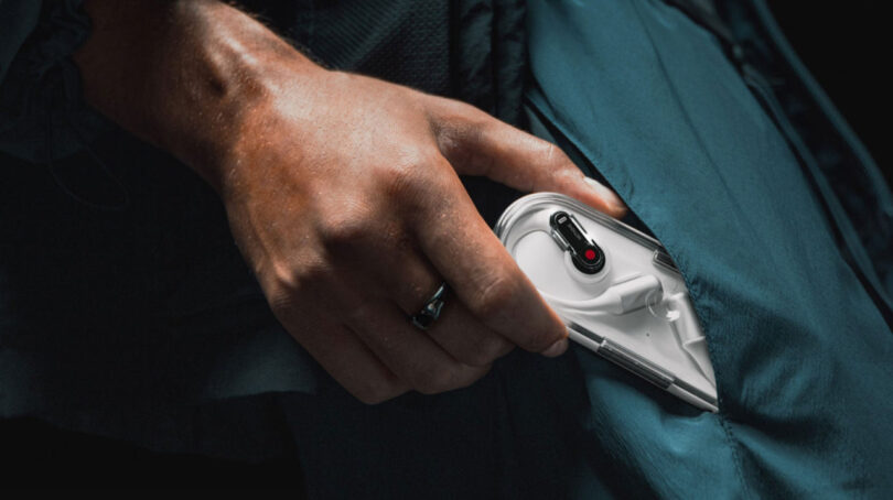 A person's hand is shown taking a white handheld device with black and red buttons out of a pocket.