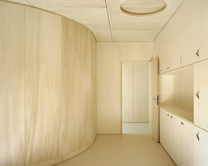 Minimalist room with light wood paneling, a curved wall, built-in cabinets, and an open door leading to another space. Ceiling features a circular light fixture.