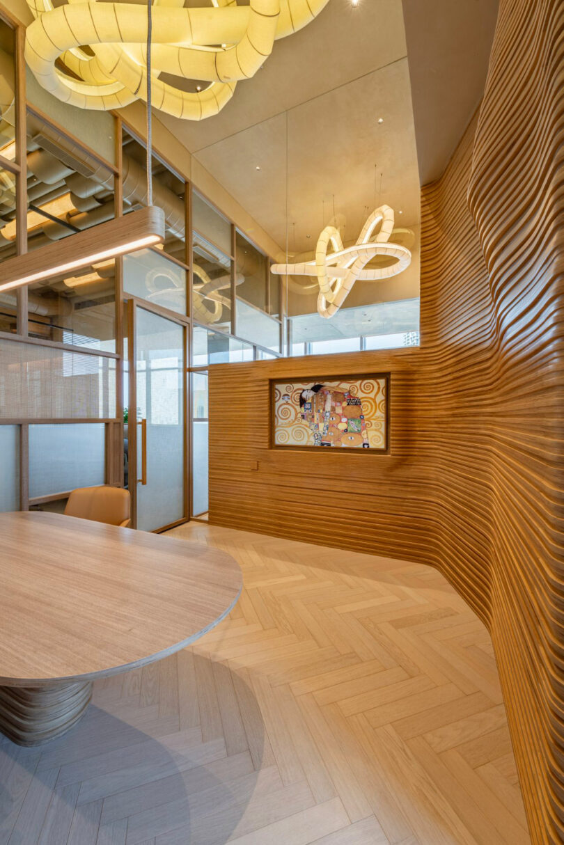 Modern office with wooden walls, a circular conference table, and artistic light fixtures. A bulletin board with various pinned items is mounted on the wavy wooden wall. Glass partitions are in the background.