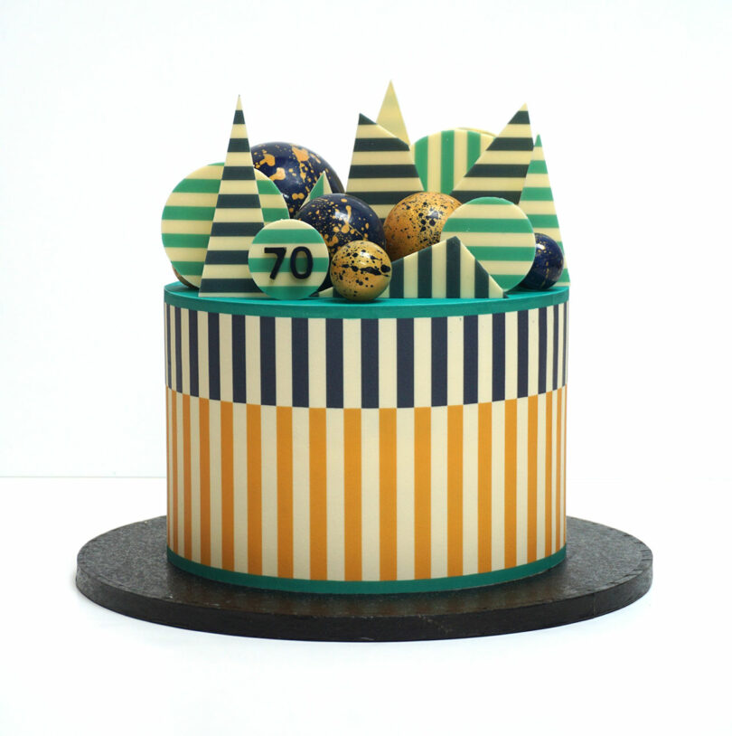 A striped cake with geometric chocolate decorations and a "70" on one piece, featuring colors like green, yellow, and blue.