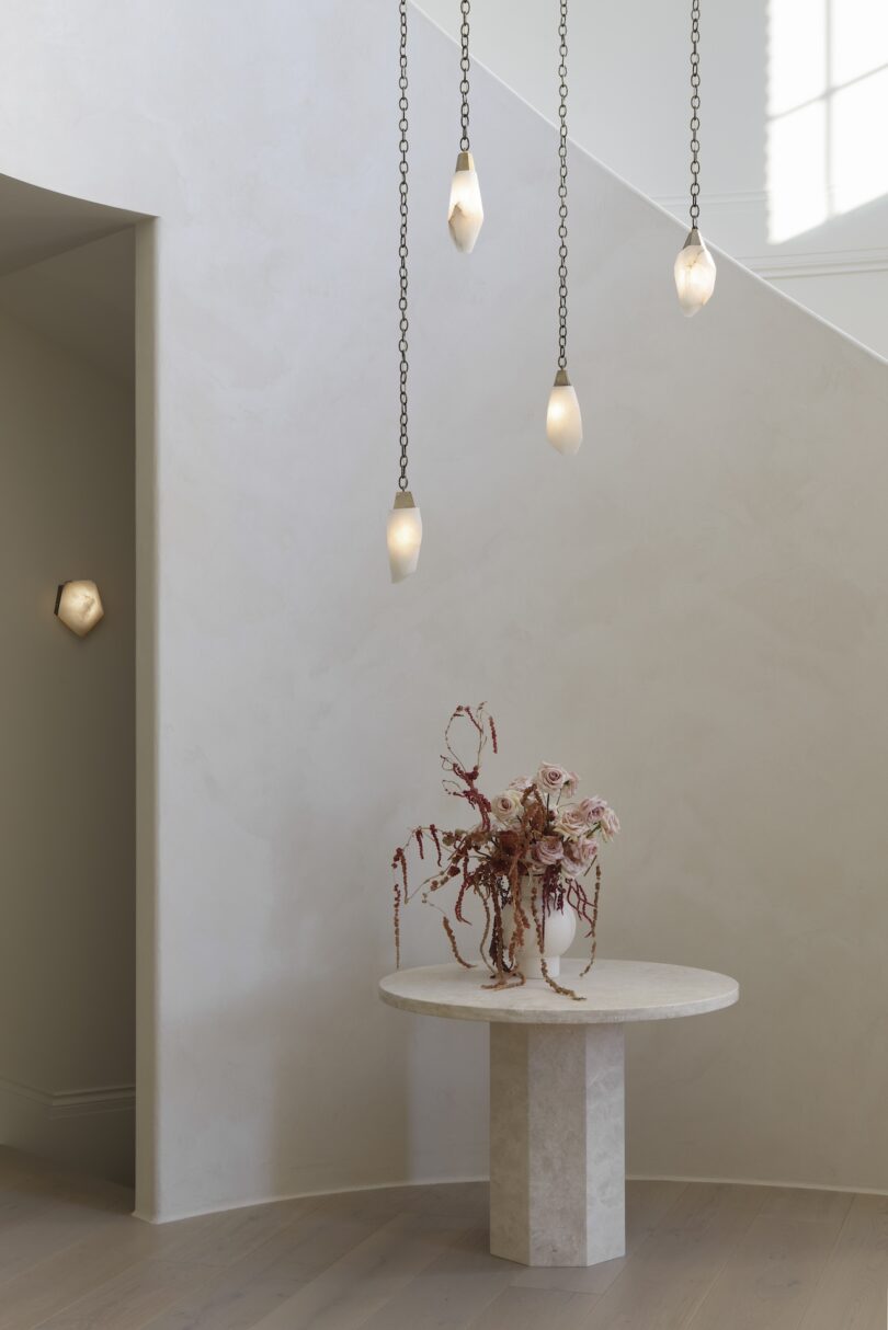 A minimalist entryway with a round table holding a floral arrangement, under five hanging teardrop pendant lights.