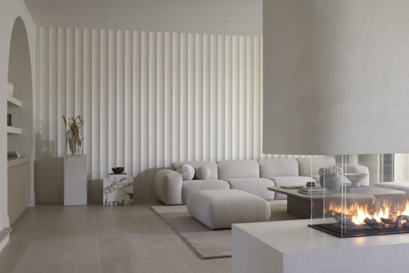 Modern living room with a glass fireplace, white furniture, textured wall, and decorative elements on shelves.