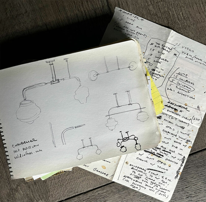 Sketches of chandeliers on an open notebook, accompanied by handwritten notes, rest on a wooden surface—a scene reminiscent of Chuck Cerankosky's creative process